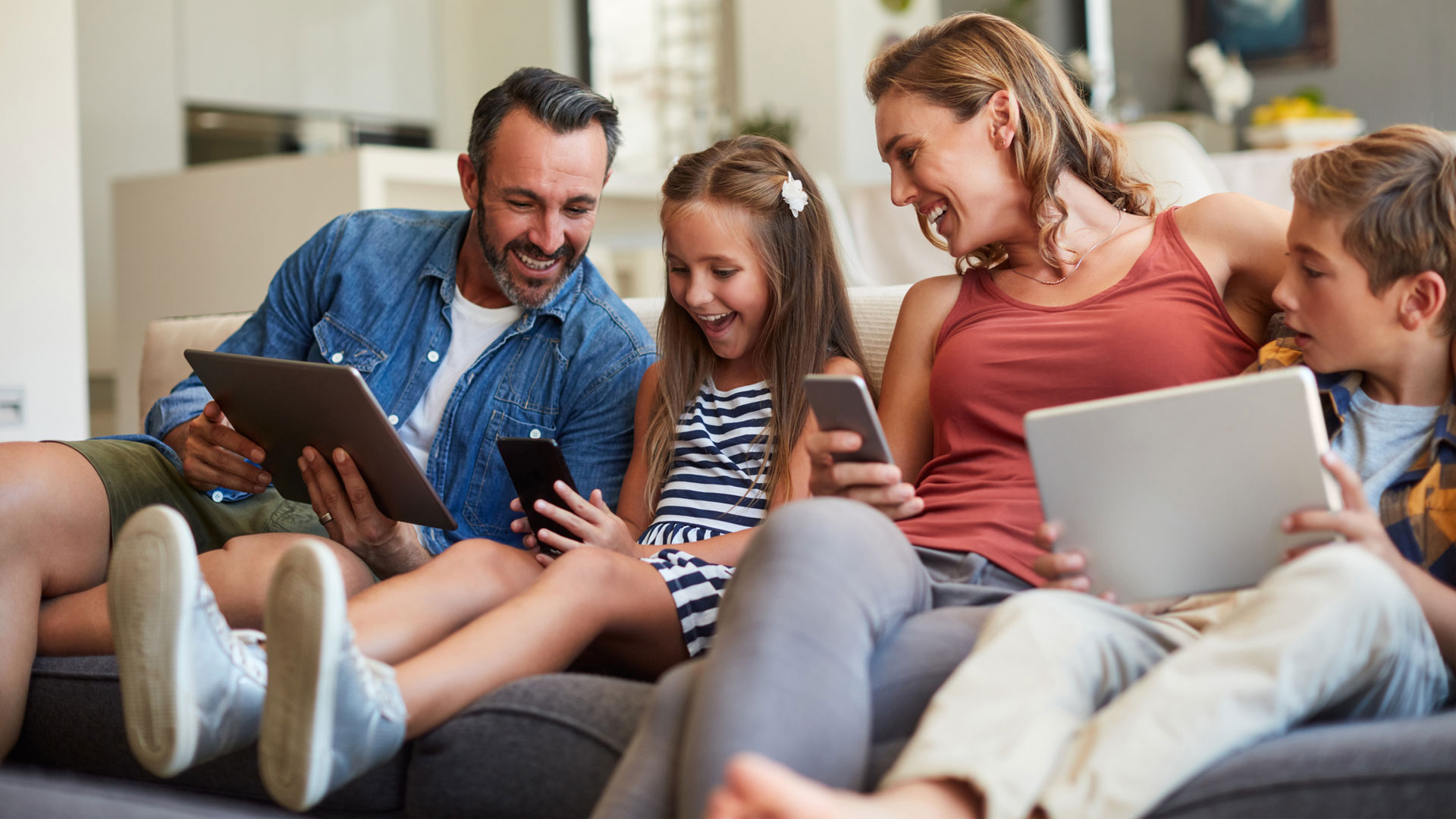 A family of four using tablets and phones, looking happy and smiling. How to Protect Your Child on Instagram 