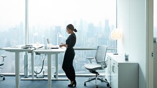 A business woman in an office standing at a desk in front of an ergonomic office chair