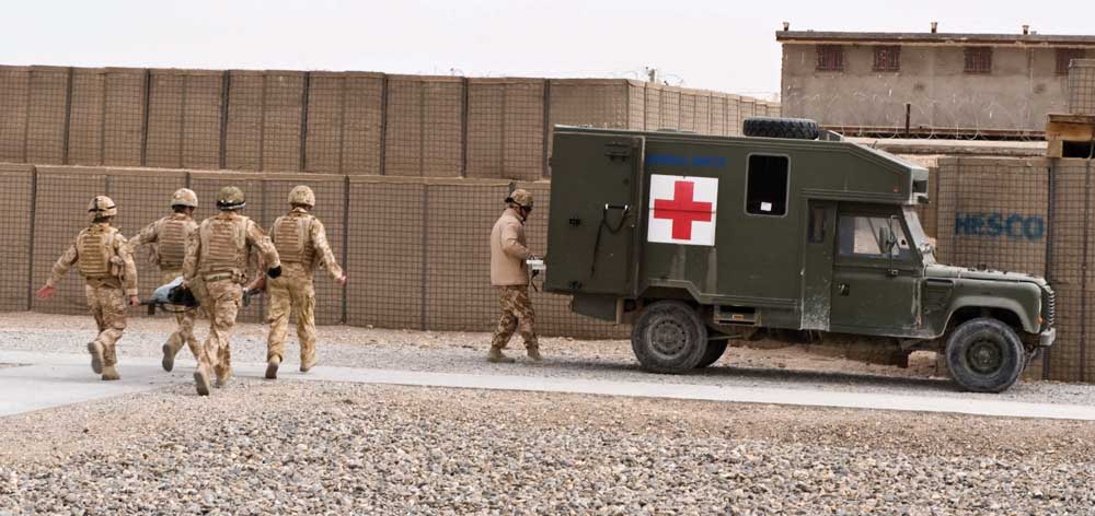 Image of army medics transporting a patient into back of an army truck with red cross logo on the side