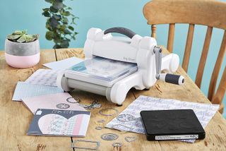 Lifestyle shot of Sizzix Big Shot Manual, one of the best embossing machines, on a cluttered crafting table
