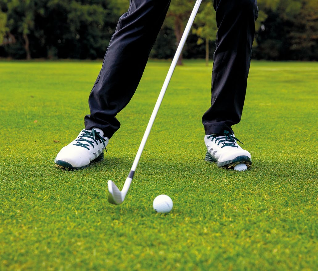 A close up image of a golfers legs and feet, with a golf ball placed under the lead foot in order to encourage pressure in this area through impact