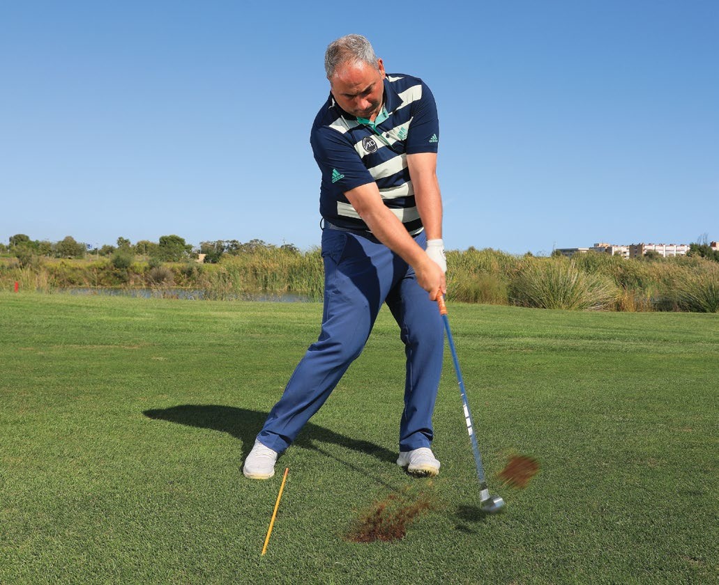 Golf coach just past impact with in the golf swing, with an alignment stick on the ground on the inside of the trail foot