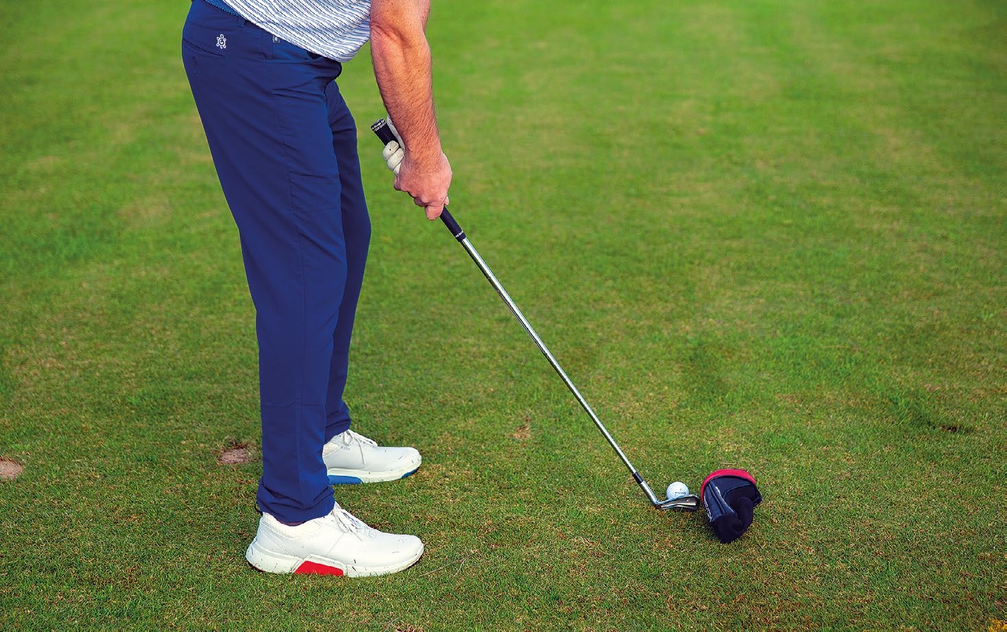 A golfer setup in a drill where a driver headcover is placed on the outside of the golf ball, with the intention of missing the headcover when swinging (which will prevent a shank)
