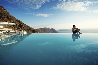 Man sits on edge of infinity pool, Santorini, Greece by PeskyMonkey