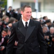 a white man wearing a black tuxedo posing in front of paparazzi on a red carpet