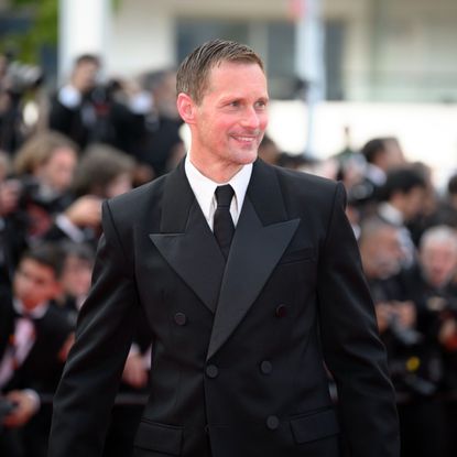 a white man wearing a black tuxedo posing in front of paparazzi on a red carpet 