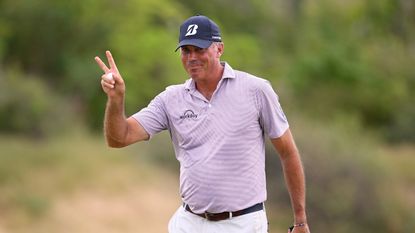 Matt Kuchar waves to the crowd with a peace sign and a golf ball in his hand at the World Wide Technology Championship 2023