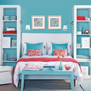 Blue bedroom with white built in shelves and wardrobes, double bed with pink and turquoise cushions and throws, blue table, wall mounted lights, IH 08/2013 Pub Orig