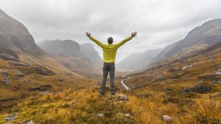 eco camping: A hiker throws his arms out wide as he looks out over Glencoe in Scotland