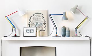 A white wall shelf with three desk lamps on it with different coloured necks.