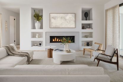 living room with modern fire lit and white sofas with pale wood floor and white walls