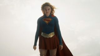 A look at Kara's blue and red suit in the Supergirl movie. She's in the air embracing a yellow sun. 