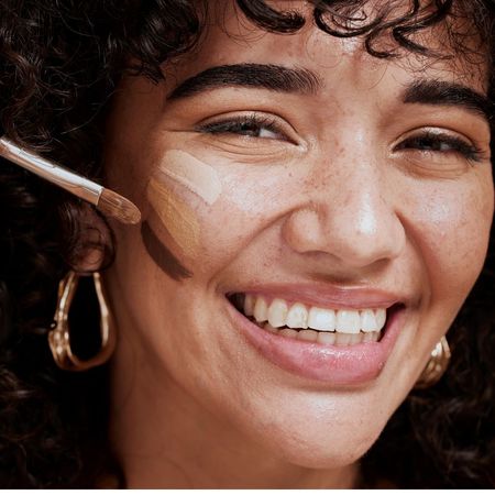 tarte concealer - smiling woman with three different shades of concealer on her cheek - gettyimages 1442518256