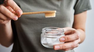 woman holding bowl of whitening powder toothpaste and toothbrush