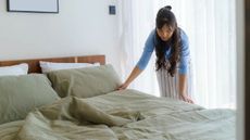 A woman with long dark hair makes her bed first thing in the morning