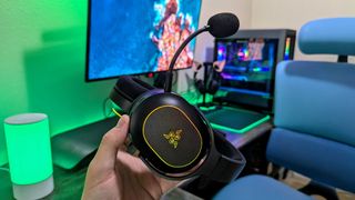 A Razer Barracuda X Chroma headset held in the hand, highlighting its detachable microphone.