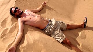 A skinny white man lies shitless on a sand dune