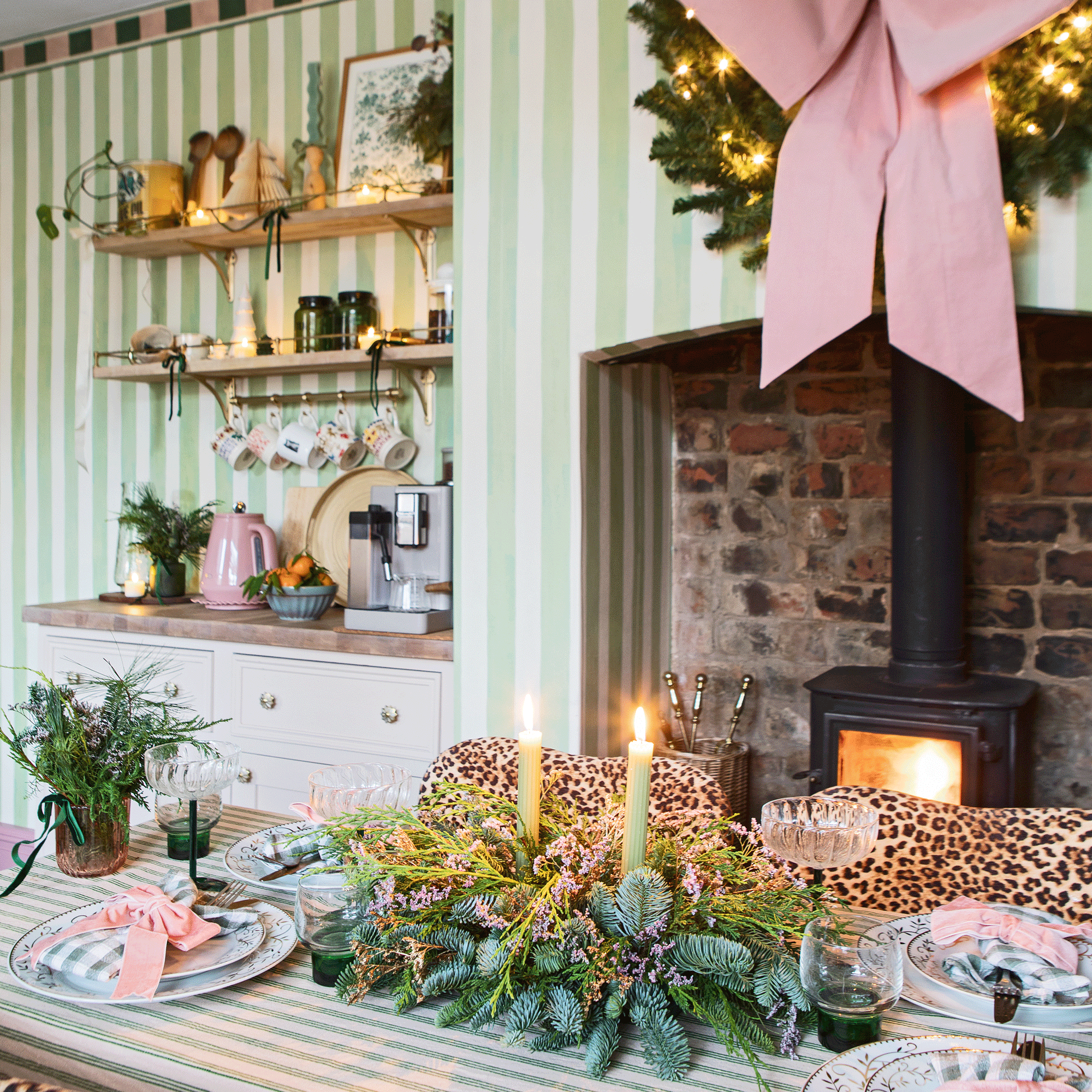 a kitchen diner with a woodburner, large decorative pink bows, green and white striped wallpaper, a dining table with a matching tablecloth and dining chairs upholstered in leopard print fabric