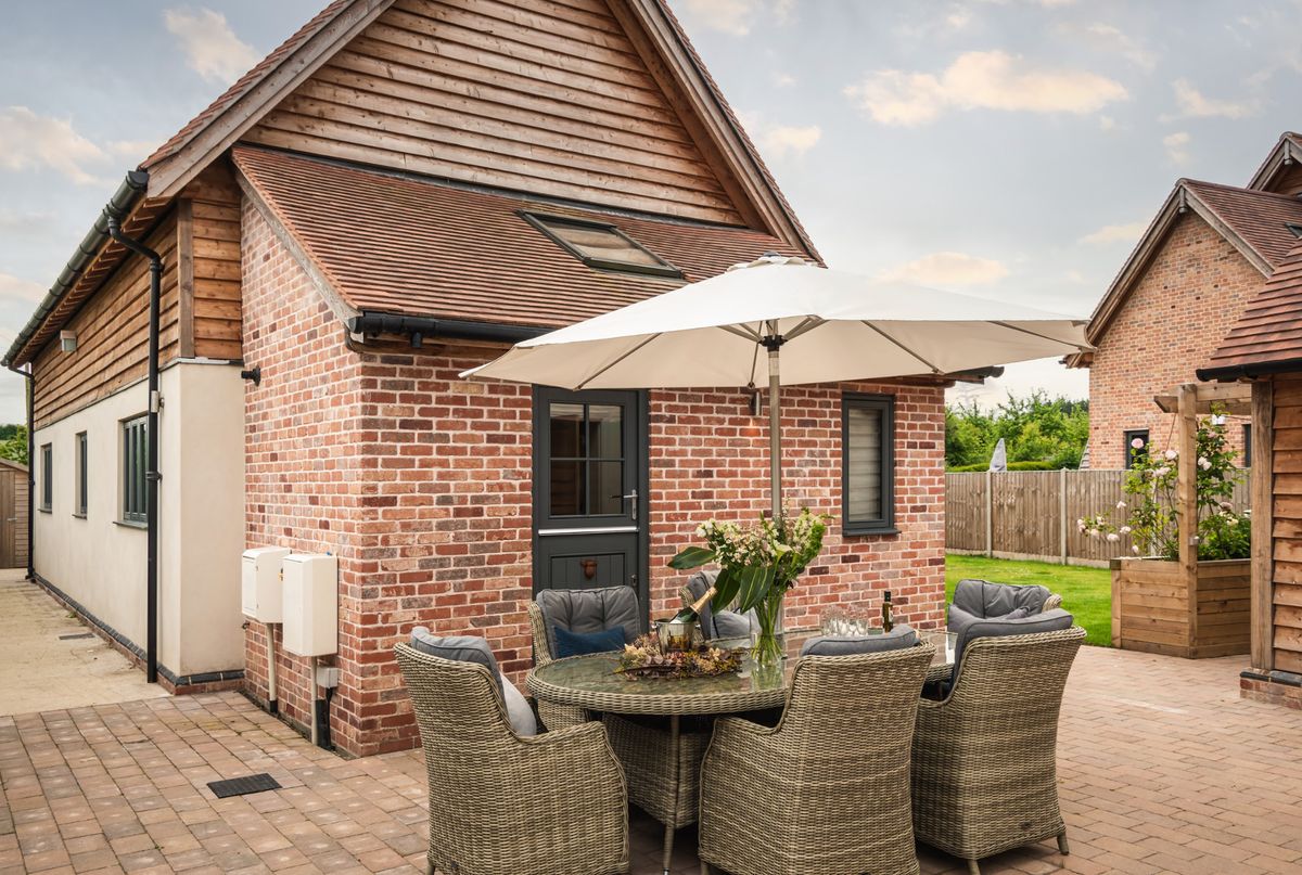 A patio with an outdoor table and chair set, topped with a parasol, wine bottle and a vase of flowers