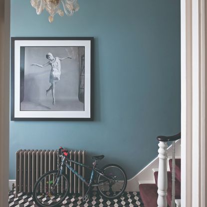 A blue hallway painted in Farrow & Ball's Inchura Blue with a black radiator and graphic tiled floor
