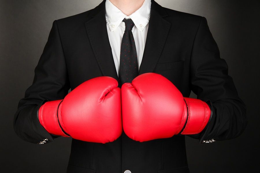 Businessman in suit &amp;amp; tie wearing red boxing gloves