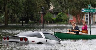 People paddle by in a canoe next to a submerged Chevy Corvette in the aftermath of Hurricane Ian in Orlando, Florida on September 29, 2022.