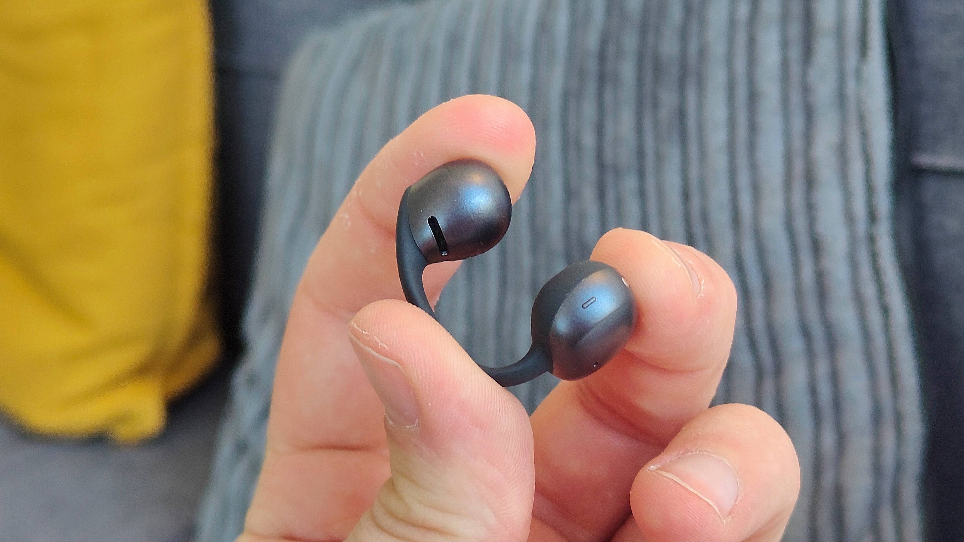The Shokz OpenDots Air in a man's hand, being slightly stretched.