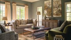 A green living toom, with a cream two-seater sofa, a green sofa opposite it, and a leather-topped coffee table in the center of them. 