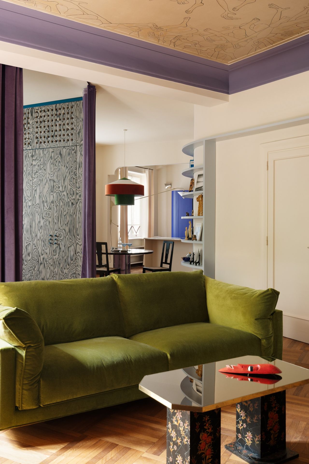 A living room with green sofa, parquet flooring, a tiger-style chair and mural painted on the ceiling