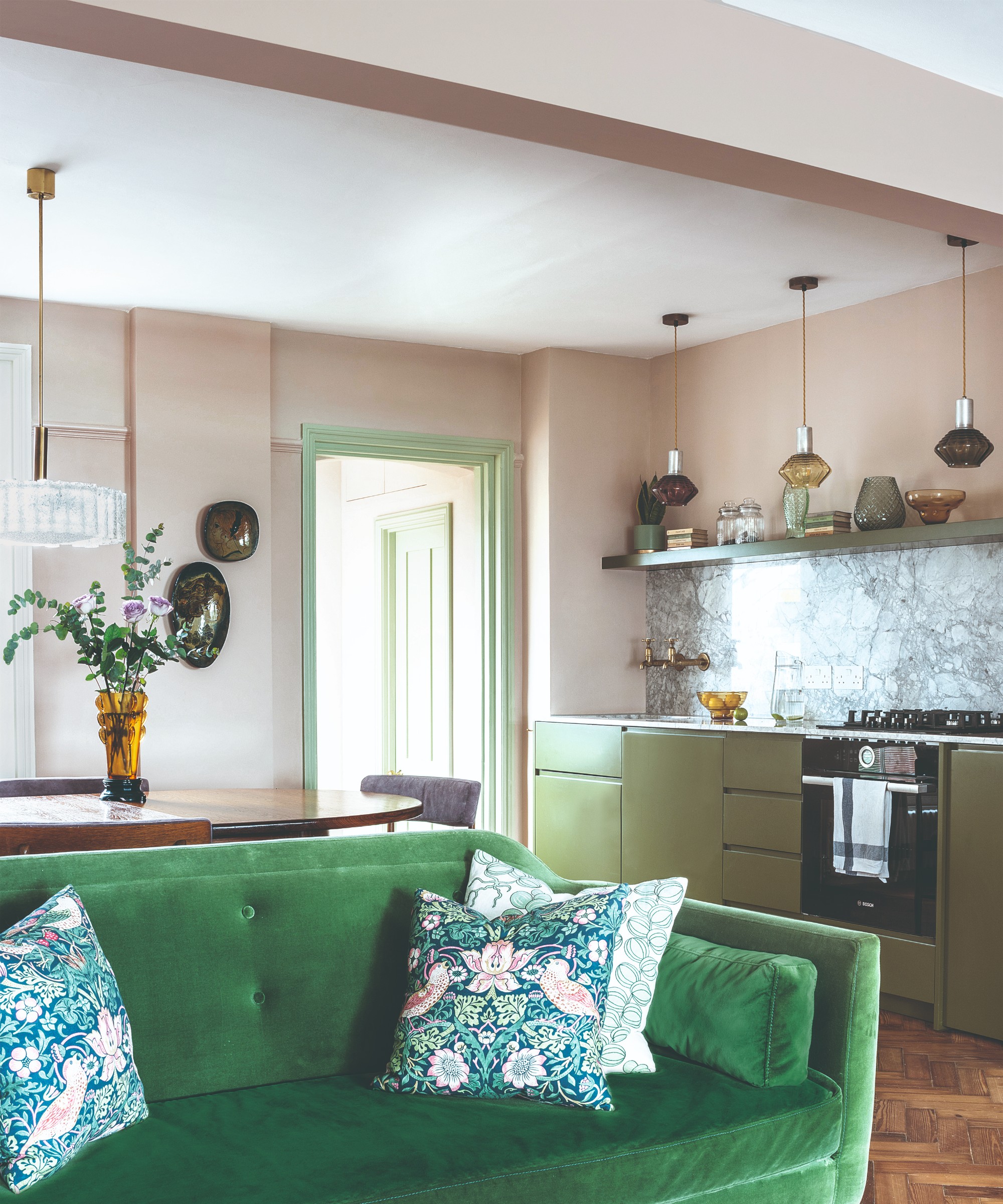 Una cocina de planta abierta pintada de rosa rosa con sala de estar con un sofá de terciopelo verde