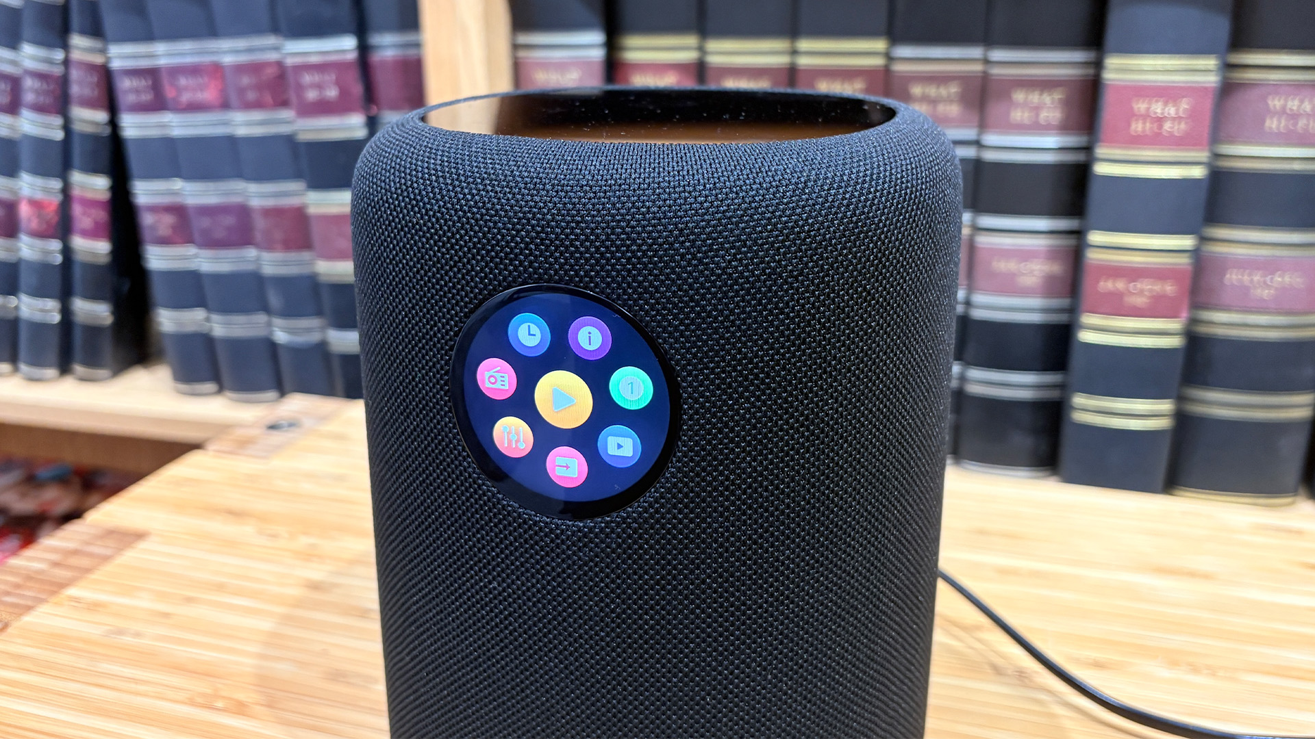 WiiM Sound wireless speaker on wooden hi-fi rack showing apps on display