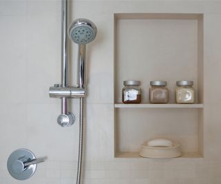 small shower head on riser in bathroom with cream tiles and small inbuilt shelf