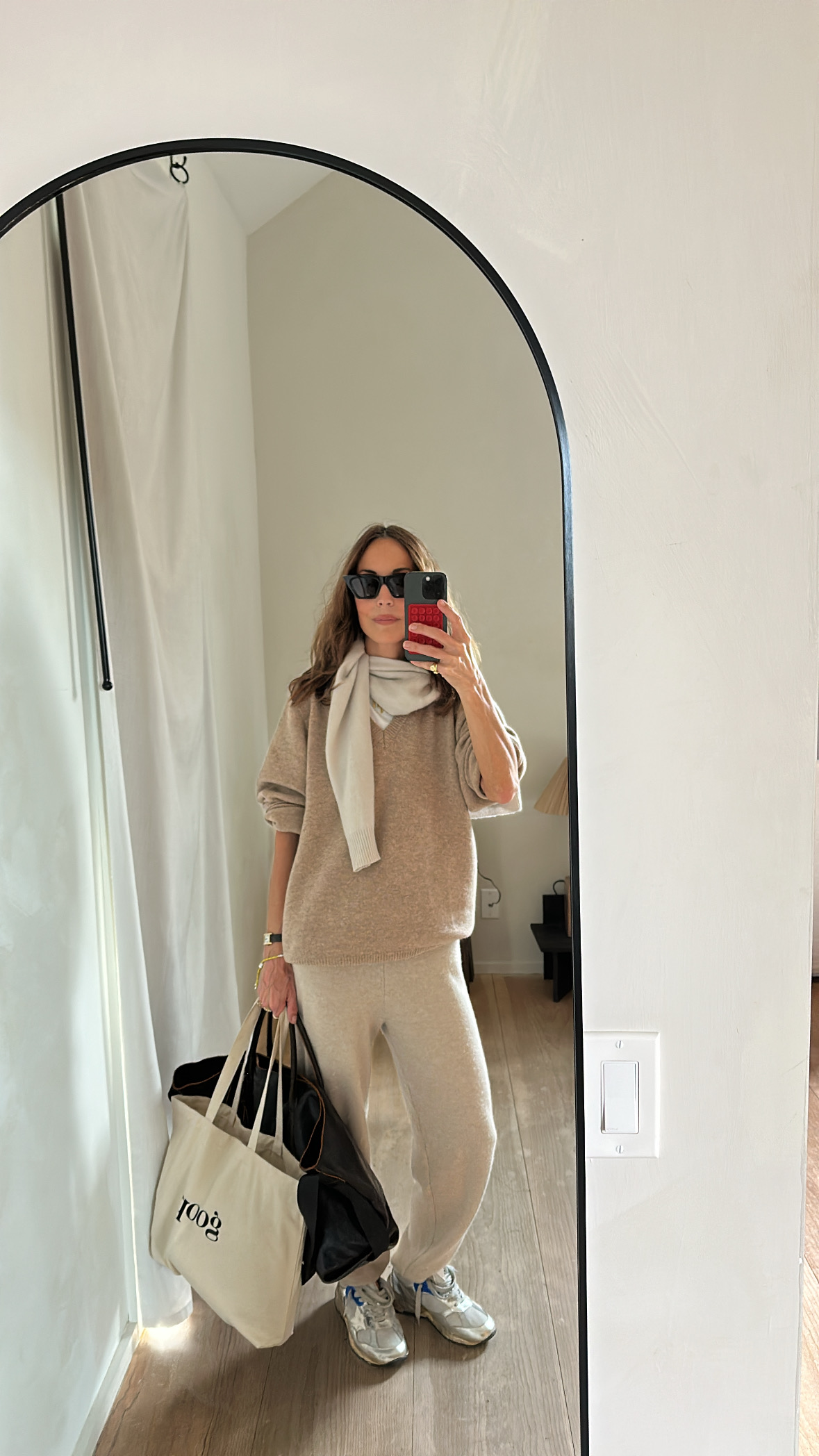Larissa Mills wearing a brown sweater, tan sweatpants, white, skirt, grey silver sneakers, a black leather tote bag, and a canvas tote bag.