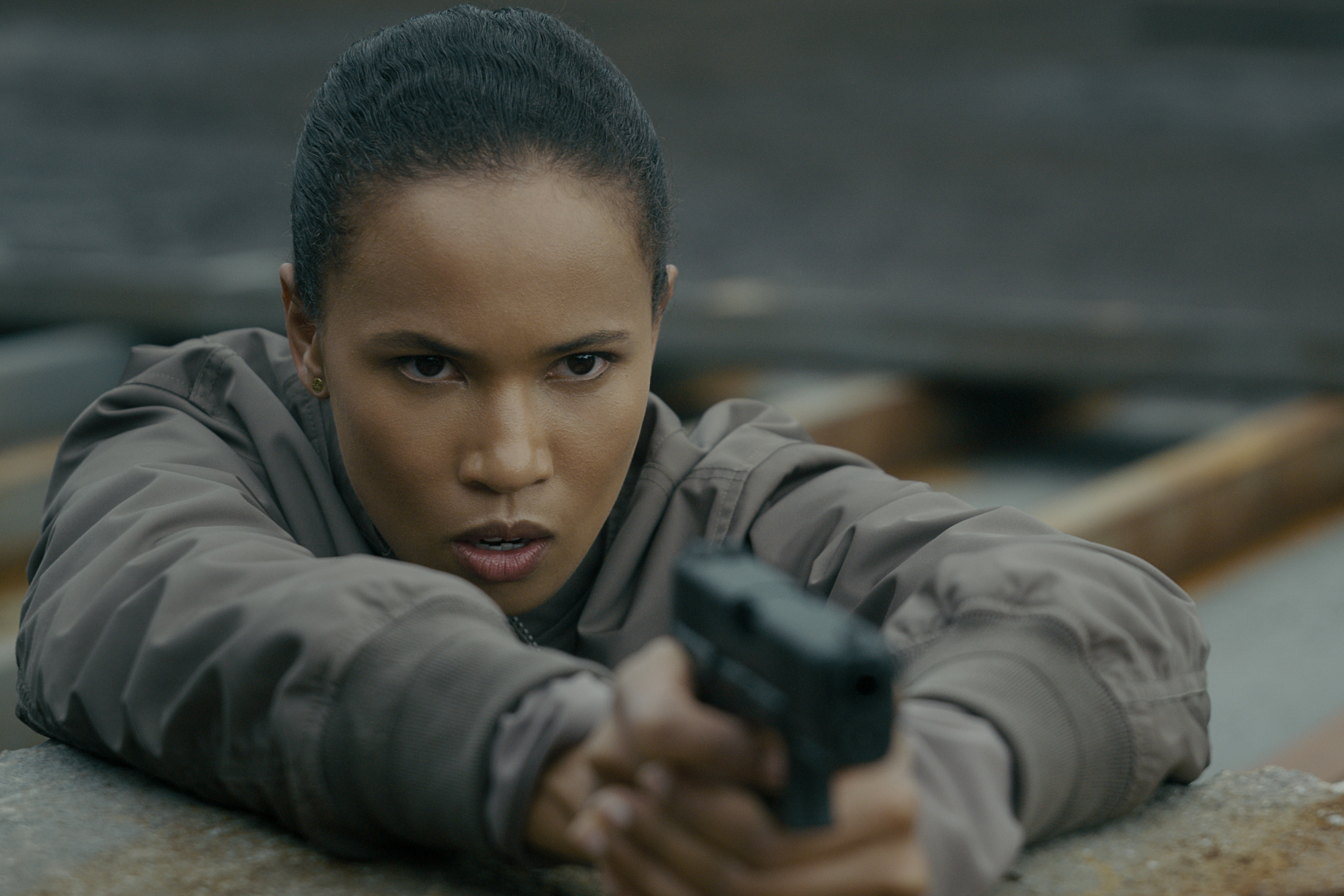 Fola Evans-Akingbola as Chelsea Arrington in episode 309 of The Night Agent lying on her stomach pointing a gun about to shoot