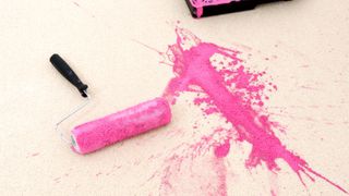 Roller and tray with pink paint spilt on cream carpet