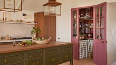 A white and green kitchen with pink wood and glazed doors leading to a walk-in pantry