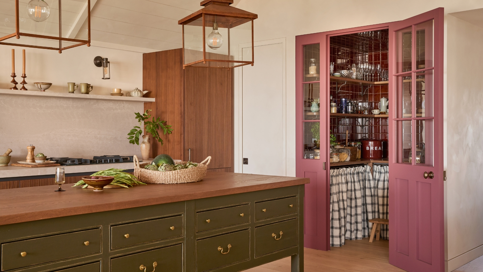 A white and green kitchen with pink wood and glazed doors leading to a walk-in pantry