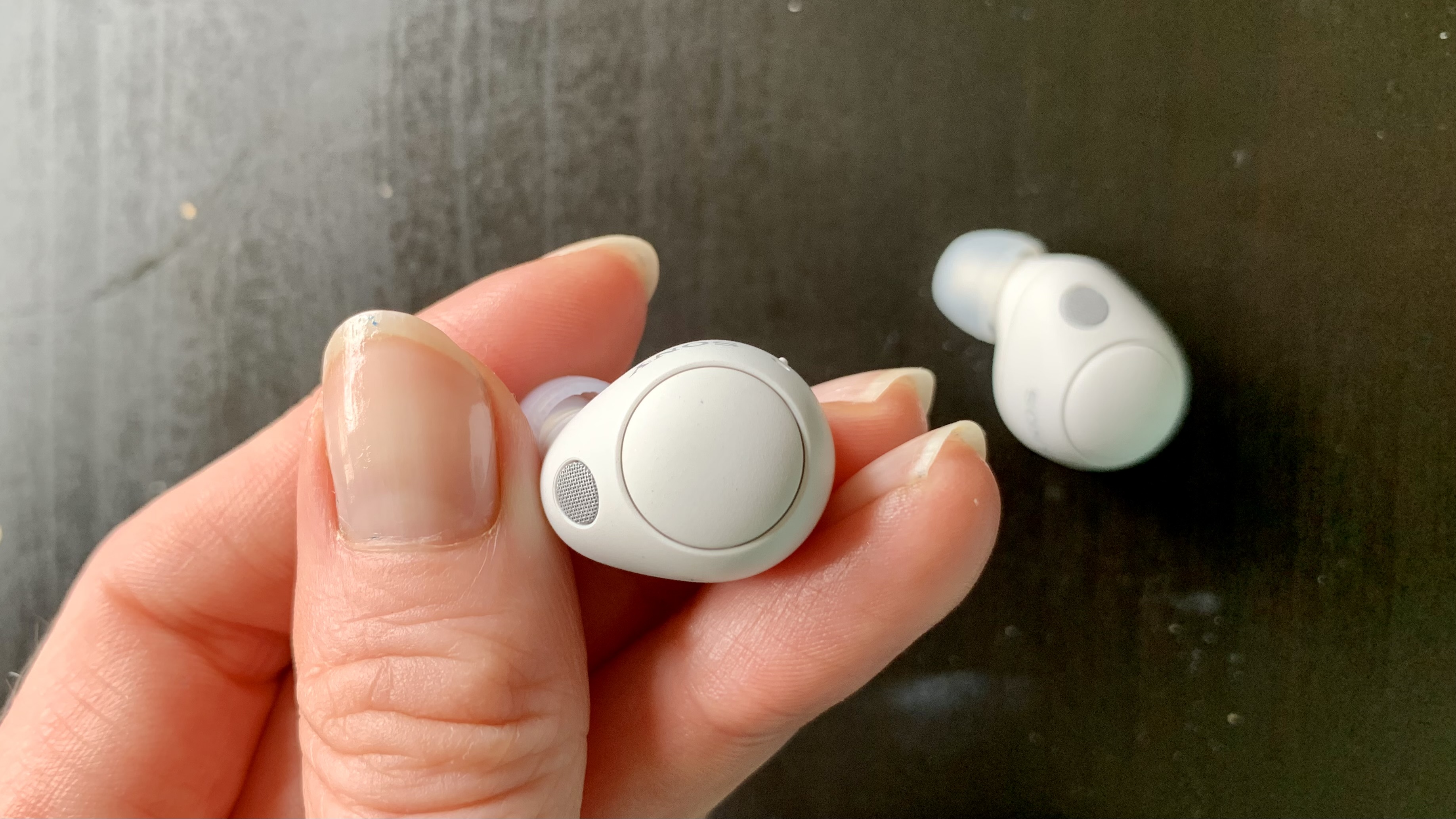 Sony WF-C700N earbuds close-up in a hand, on gray background