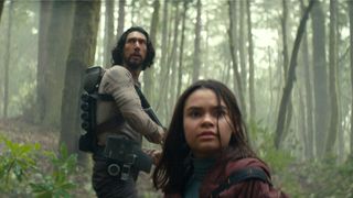Mills (Adam Driver), weapon in hand, with Koa (Ariana Greenblatt) in the foreground in 65