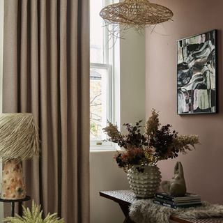 A pink themed living room with long pink curtains to the floor and a small wooden side table