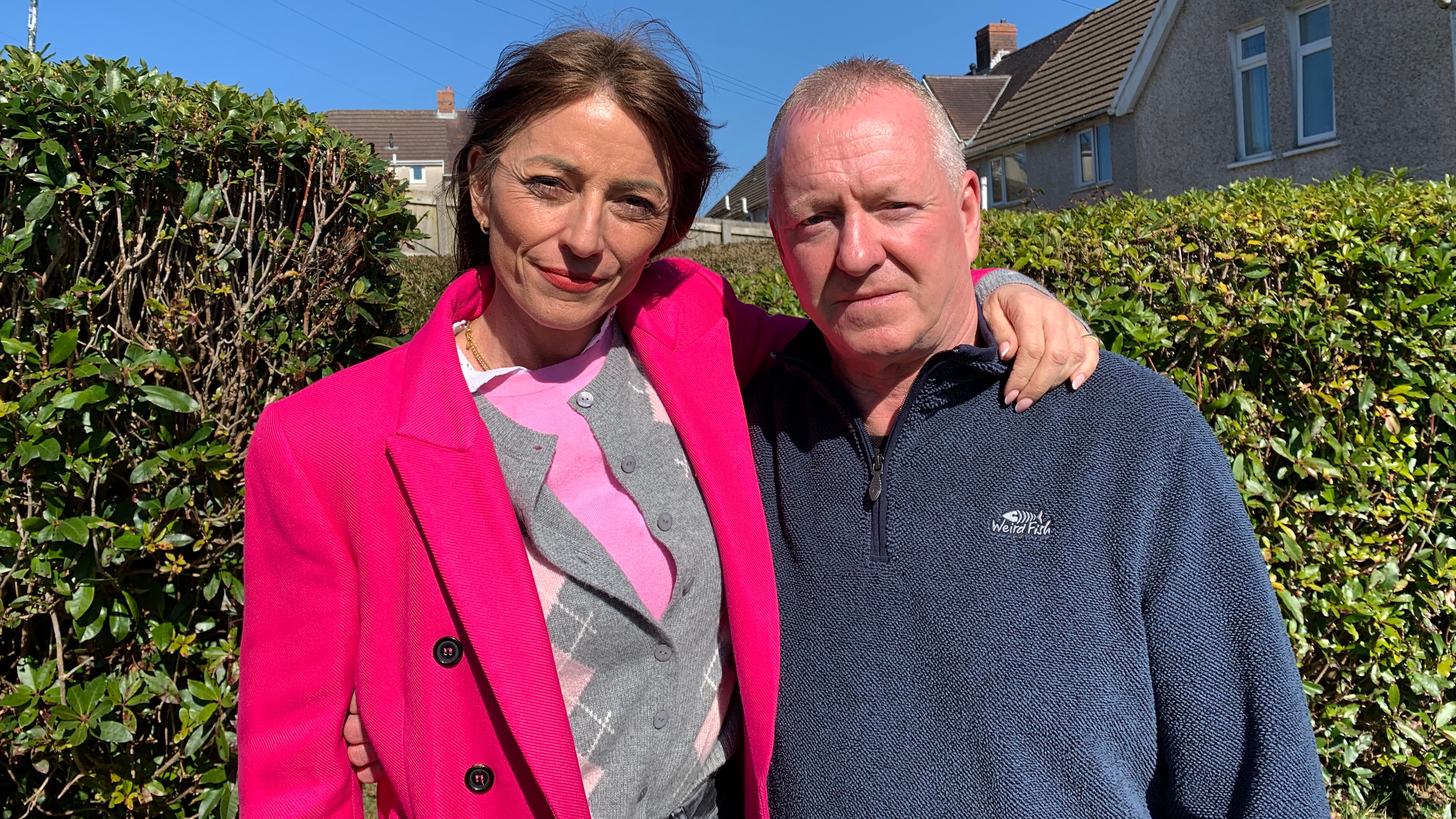 Davina McCall in a bright pink coat standing in a garden with and Simon Prothero who is in a navy fleece.