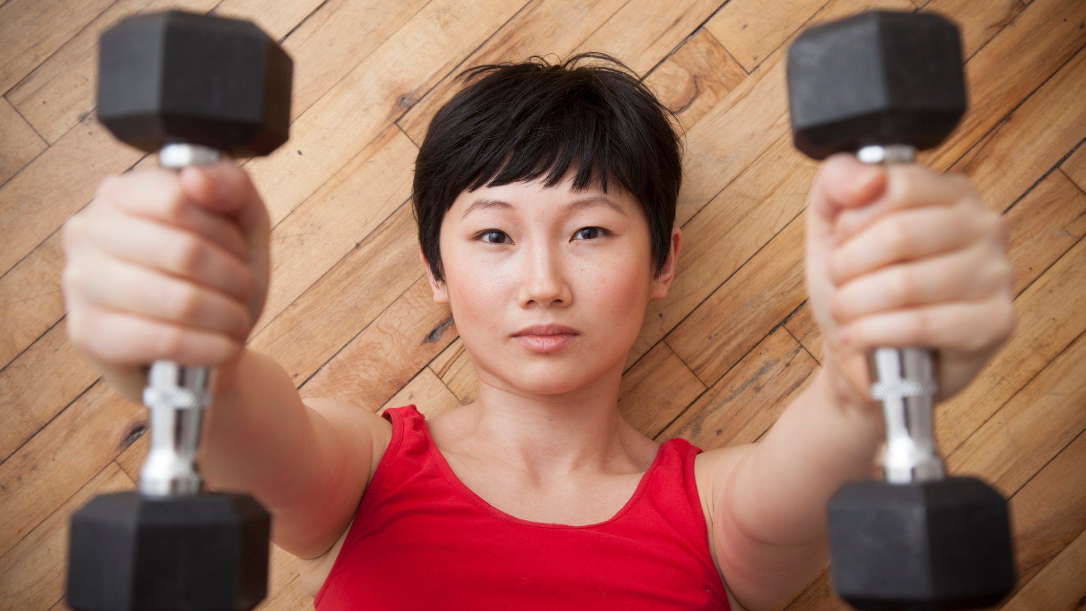 Woman lying on wooden floor holding dumbbells above her