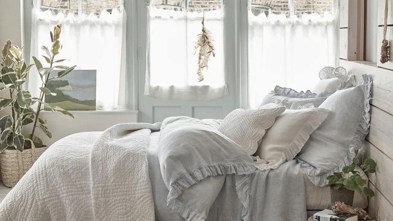 A bed styled with multiple light colored linens and pillows