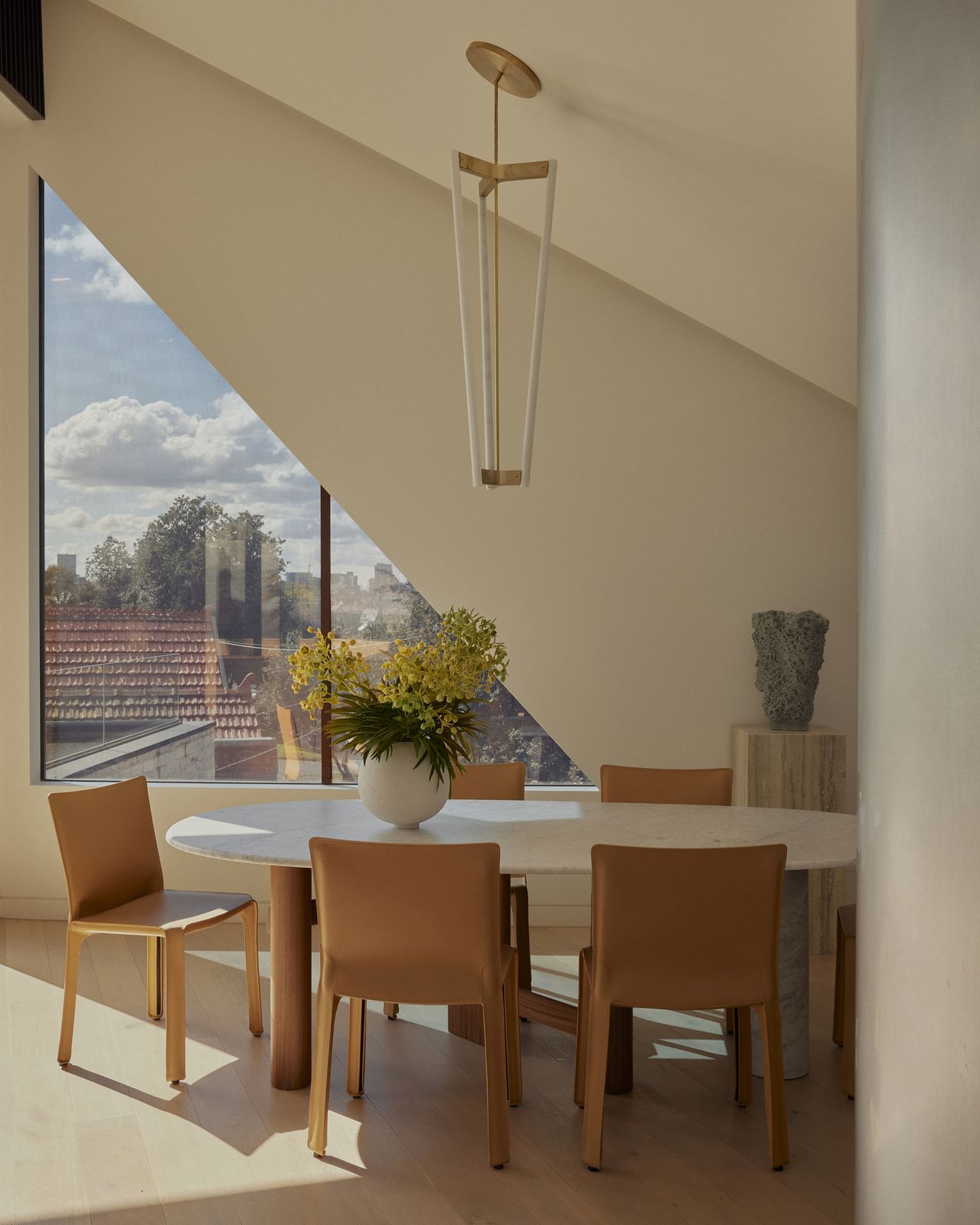 modern dining room with sloped ceiling, sculptural light hanging over dining table, leather dining chairs and a marble plinth with vase on it