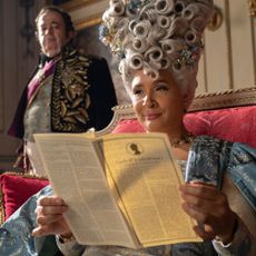 queen charlotte smirking as she reads the society papers on her throne in bridgerton