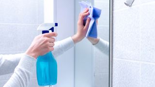 Someone cleaning a bathroom mirror with a microfiber cloth and spray bottle