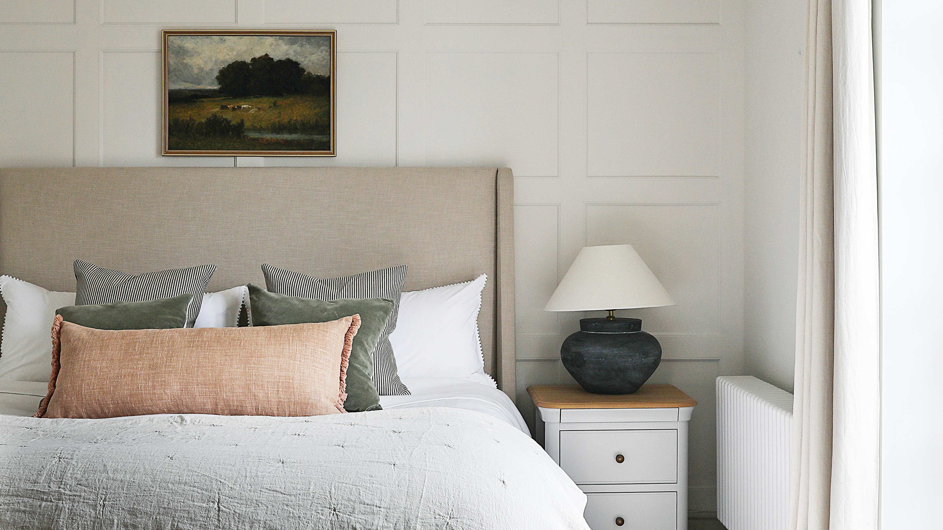 A cream bedroom with a taupe headboard and bed dressed in neutral bed linen