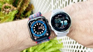 Apple Watch Series 10 next to a Garmin Forerunner 570 on a user's wrist with green foliage out of focus in the background