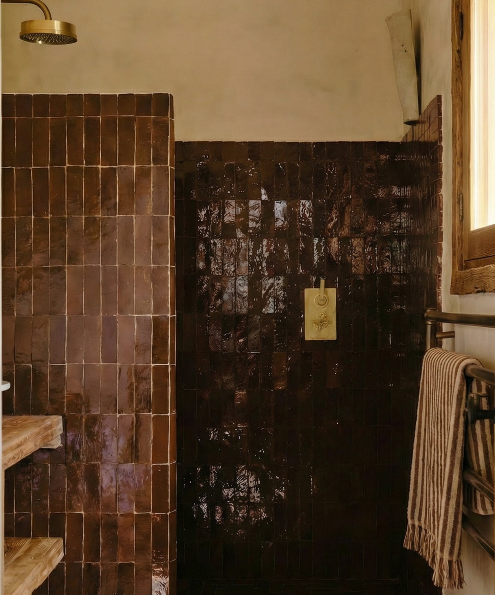 A walk in shower clad in dark brown zellige tiles, light brown walls, and brown bathroom accessories