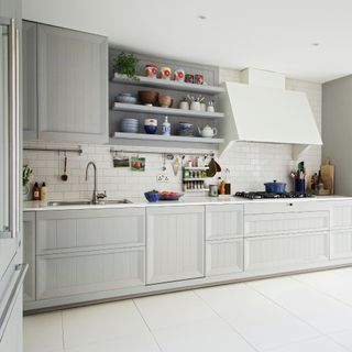 White fitted kitchen with open shelves and extractor hood and wooden table in contemporary retro kitchen